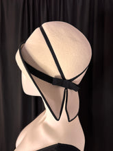 Load image into Gallery viewer, Side view: Winter white cloche hat with black grosgrain ribbon trimmings and a bow at the brim’s split. Designed by Mr John Jr in the 1960s. A minimalist’s dream!

