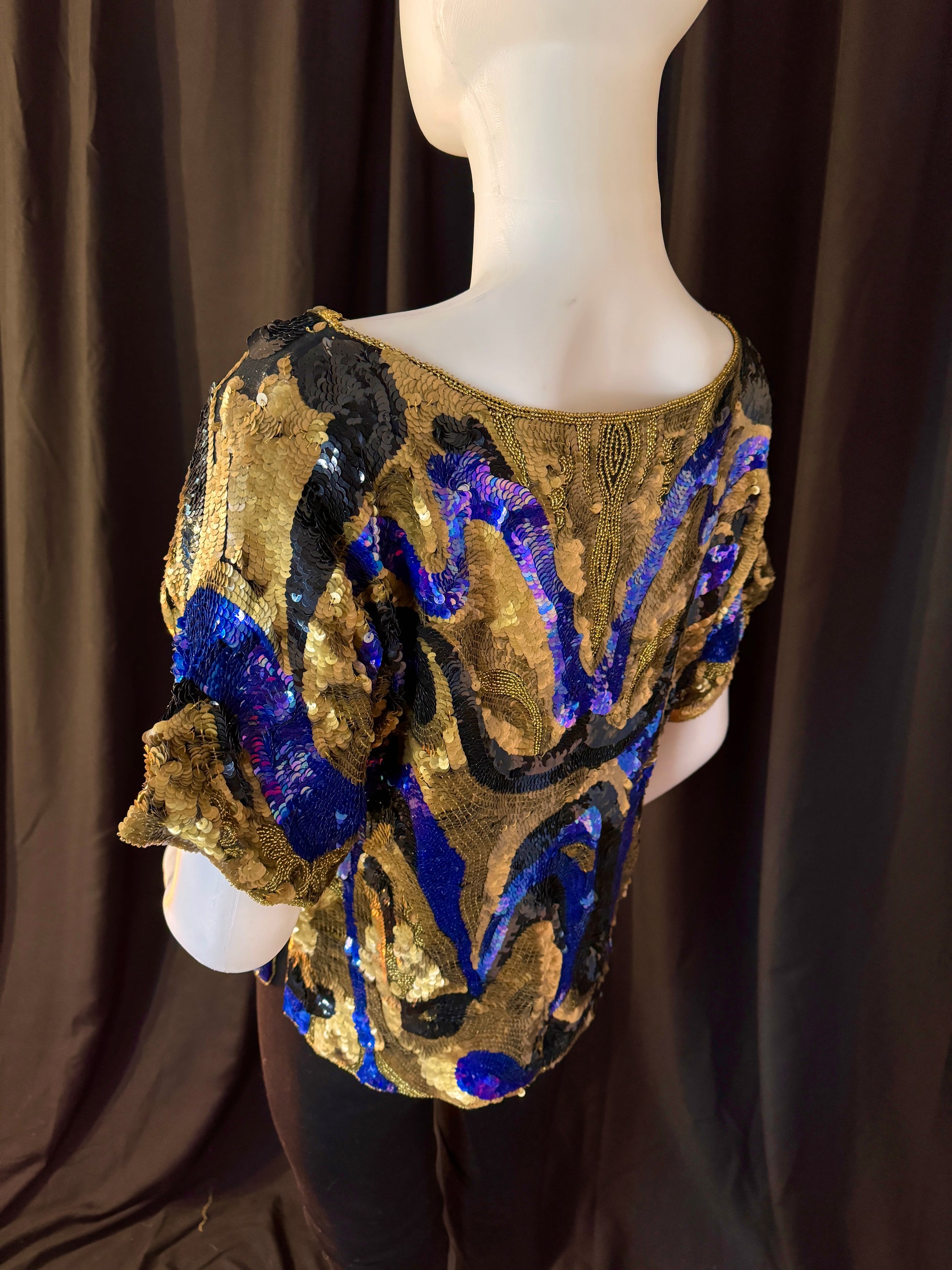 Oleg Cassini sequined top, back view on Mannequin with emphasis on blue and black swirling pattern against gold background. 