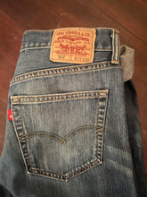 Load image into Gallery viewer, View of back pocket and Levi&#39;s 501 label. The jeans are pre-owned in good condition with distress hems.

